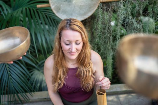 Yoga concept, meditation and sound therapy. Beautiful young caucasian woman surrounded by copper tibetan singing bowls and instruments.
