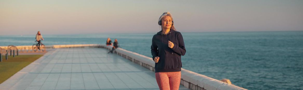 Mature woman in sportswear running along the seashore in the evening