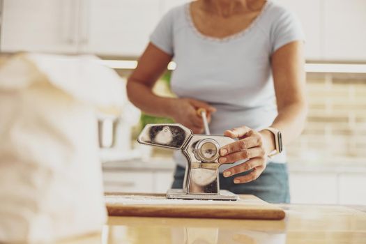 A woman standing in the kitchen at the table cuts noodles in a noodle cutter
