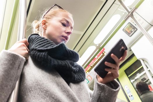 Young woman passenger using smartphone while moving in the modern metro, commuting by public transport