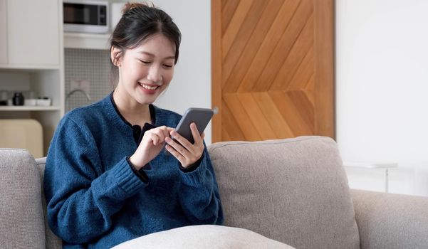 Portrait beautiful young asian woman use smart mobile phone on sofa in living room interior