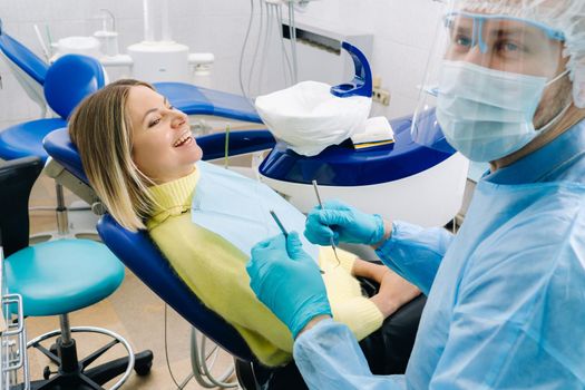 The patient smiles in the dentist's chair in a protective mask and instrument before treatment in the dental office