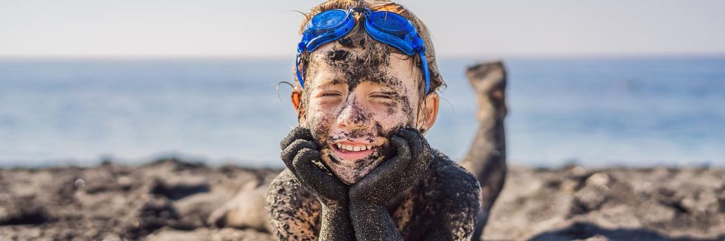 BANNER, LONG FORMAT Black Friday concept. Smiling boy with dirty Black face sitting and playing on black sand sea beach before swimming in ocean. Family active lifestyle, and water leisure on summer vacation with kids. Black Friday, sales of tours and airline tickets or goods