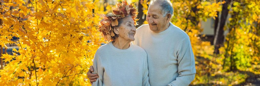 Happy old couple having fun at autumn park. Elderly man wearing a wreath of autumn leaves to his elderly wife BANNER, LONG FORMAT
