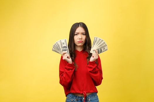 Young woman over yellow wall holding dollars stressed with hand on head, shocked with shame and surprise face, angry and frustrated. Fear and upset for mistake.