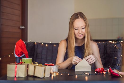 Young woman is packing presents. Present wrapped in craft paper with a red and gold ribbon for christmas or new year. Woman makes an advent calendar for her child