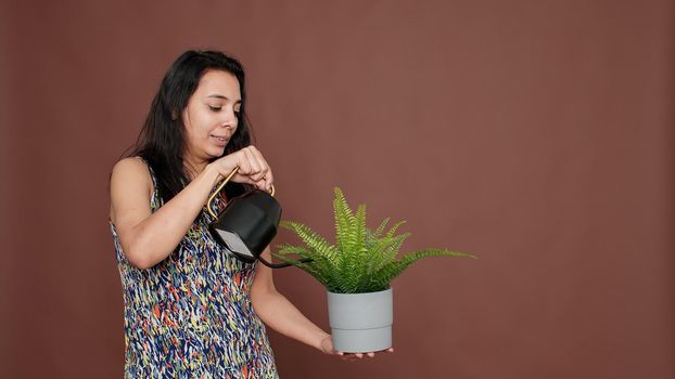 Happy model holding flowerpot and watering green plant