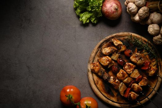 Barbecued chicken kebab with bell pepper, cherry tomato and onions on dark stone background. Copy space for your text