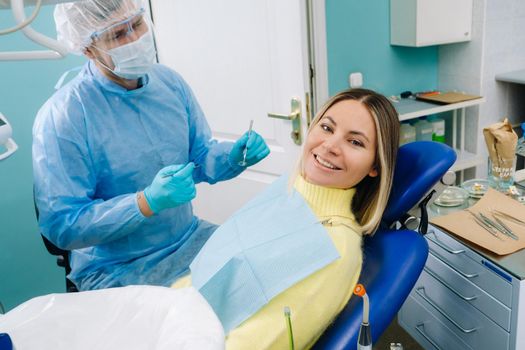 The patient smiles in the dentist's chair in a protective mask and instrument before treatment in the dental office