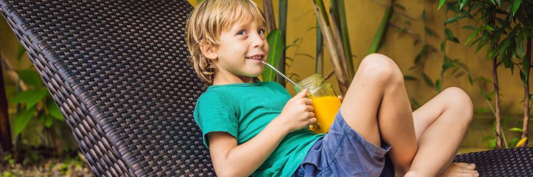 Boy drinking juicy smoothie from mango in glass mason jar with steel straw on the background of the pool. Healthy life concept, copy space BANNER, LONG FORMAT