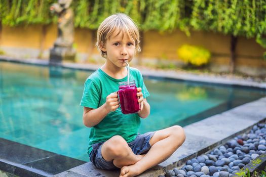 Boy drinks dragon fruit smoothie with steel drinking straw by the pool