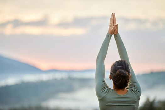 Woman practicing yoga doing warrior pose in front of foggy mountains in morning.