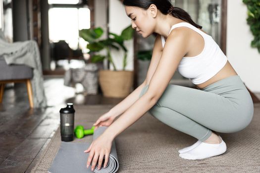 Young asian girl prepare floor mat for yoga, meditation or fitness training at home, workout in her house, wearing activewear
