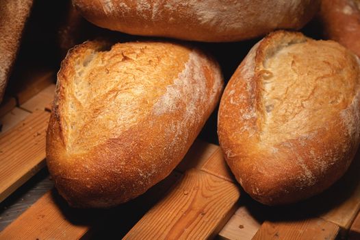 Fresh crispy hot delicious craft artisan bread. Many loaves lie on a wooden pallet