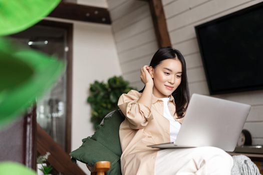 Young asian woman sitting at home with laptop computer. Girl browsing websites or studying remotely