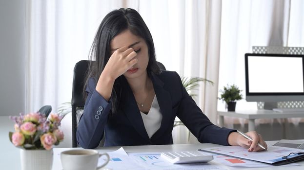 Stressed female office worker looking worried, tired and overwhelmed while working at office desk.