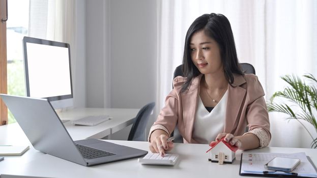 Smiling female professional investor using calculator and working with computer laptop at office desk.