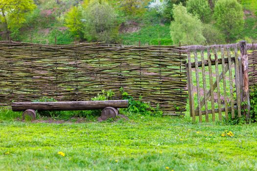 horizontal wattle fence with wicket and wooden bench near