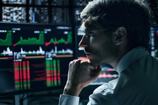 thoughtful investor looking at monitors with stock market data.
