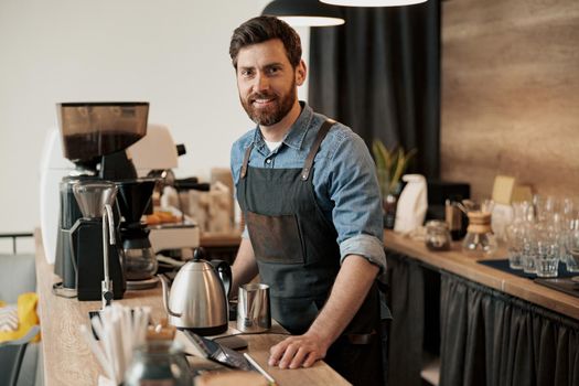 Barista with stylish beard smiling while behind a counter in the coffeeshop
