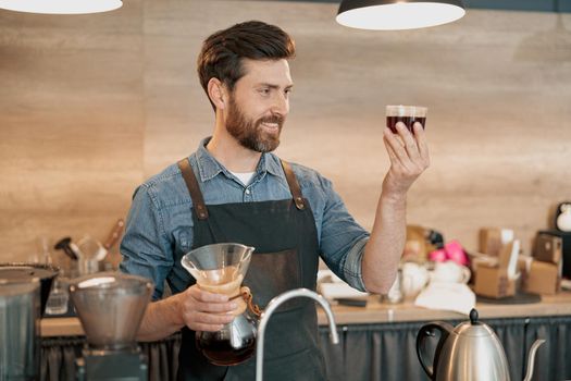 Smiling barista appraisingly looks at a glass of filter coffee