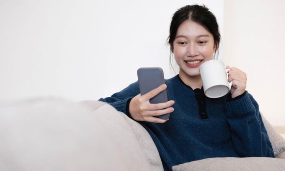 Close-up Of Smiling thailand Lady Having Cellphone Conversation And Enjoying Hot Drink While Relaxing On Couch.
