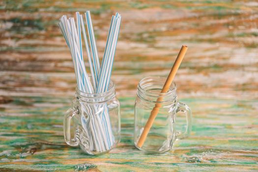 Bamboo drinking straw vs disposable straws on wooden painted background. Zero waste concept