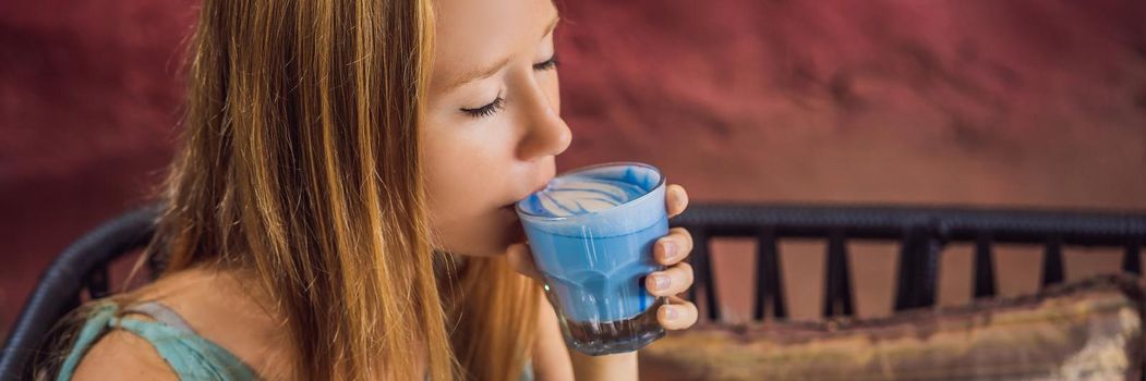 Young woman having a mediterranean breakfast seated at sofa and drinks Trendy drink: Blue latte. Hot butterfly pea latte or blue spirulina latte BANNER, LONG FORMAT