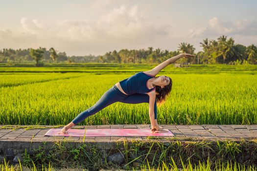 Young woman practice yoga outdoor in rice fields in the morning during wellness retreat in Bali