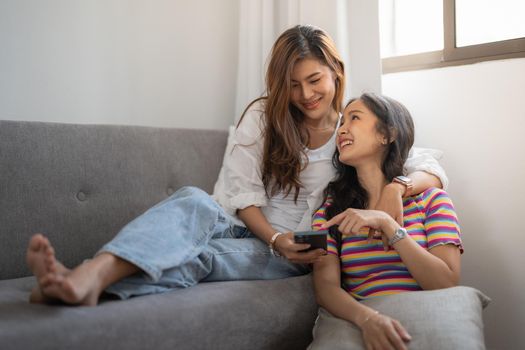 Two happy young asian casual women having fun using smartphone at home. Lesbian millennial couple concept.