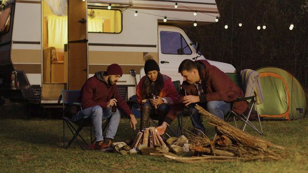 Man helping friend to light the camp fire in front of retro camper