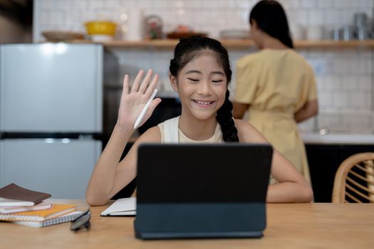 Smiling little asian girl in headphones have video call distant class with teacher using laptop, happy small child wave greeting with tutor, study online on computer, homeschooling concept