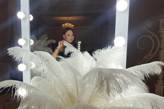 Beautiful asian young woman and decorative ostrich feathers on a gold table next to a make-up mirror.