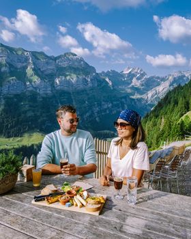 couple men and woman on vacation in the Swiss Alps Aescher cliff viewed from mountain Ebenalp in the Appenzell region in Switzerland Aescher cliff