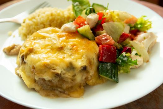 Dinner dish with large minced cutlet with yellow cheese and salad with peppers, cucumber and white cheese.