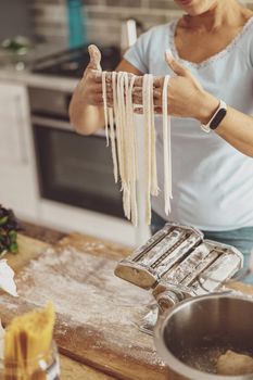 A woman holds freshly chopped long noodles near a noodle cutter