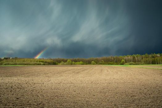Fantastic clouds with a rainbow and a ploughed field