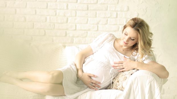 Happy pregnant woman sitting on sofa at home