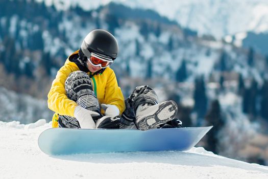 Young woman snowboarder sits in the snow and fastens fastenings on a snowboard before the descent
