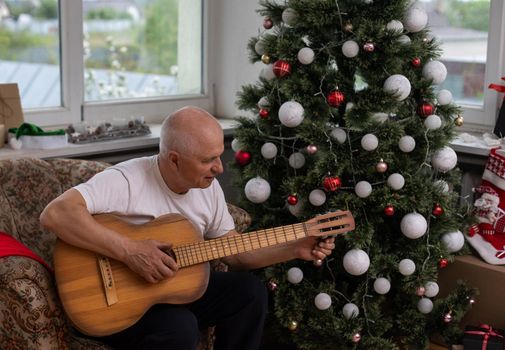 Happy people family concept - Old senior man enjoying the guitar on the sofa in the house at christmas