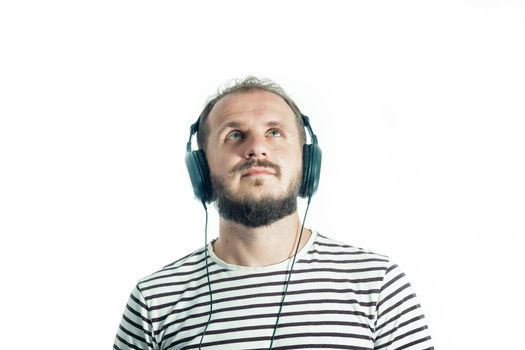 Bearded happy man in a striped T-shirt listens to music with big headphones. looking up. 30-35 years old. Isolated
