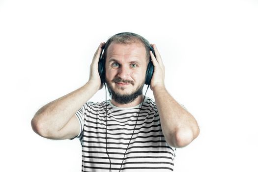 Smiling bearded happy man in a striped T-shirt listens to music with big headphones. Look at camera. Isolated on white.