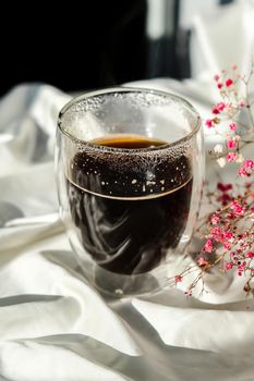 Milk pouring into the glass cup with black coffee. Morning aesthetics vibes. Breakfast. Pink gypsophila flowers