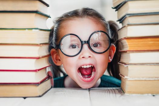 Screaming little blonde kid girl 4-6 years old in glasses in library among many books, children studio close-up portrait. Kid education concept.