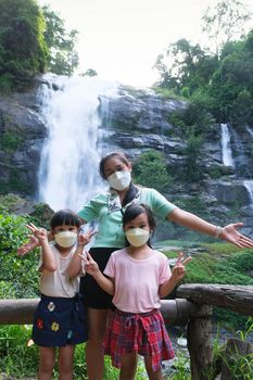 Family of Asian tourists standing near Wachirathan Waterfall looking at camera and smiling in Inthanon National Park, Chiang Mai, Thailand.