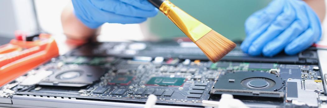 Man in gloves with a paintbrush cleans laptop parts