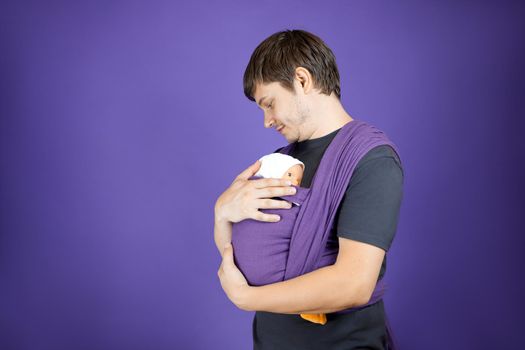 A young man is learning to be a father. Training of wearing a baby on a doll. Parenting course.