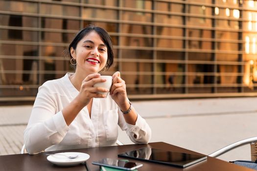 businesswoman smiling with a cup of coffee in her hands on the terrace of a coffee shop, concept of digital entrepreneur and urban lifestyle, copy space for text