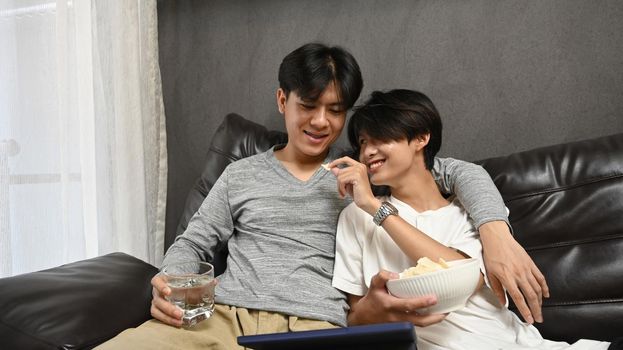 Young homosexual couple embracing and enjoying the movie on laptop. LGBT and love concept
