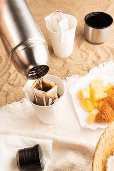 Pouring hot water through trendy convenient paper drip coffee bag into paper cup outdoors.
